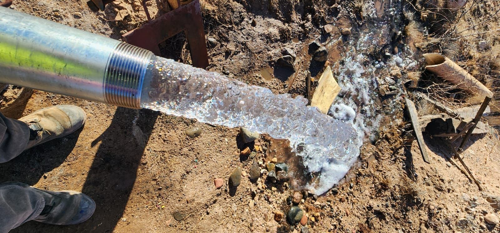 A person is pouring water from a hose into the ground.