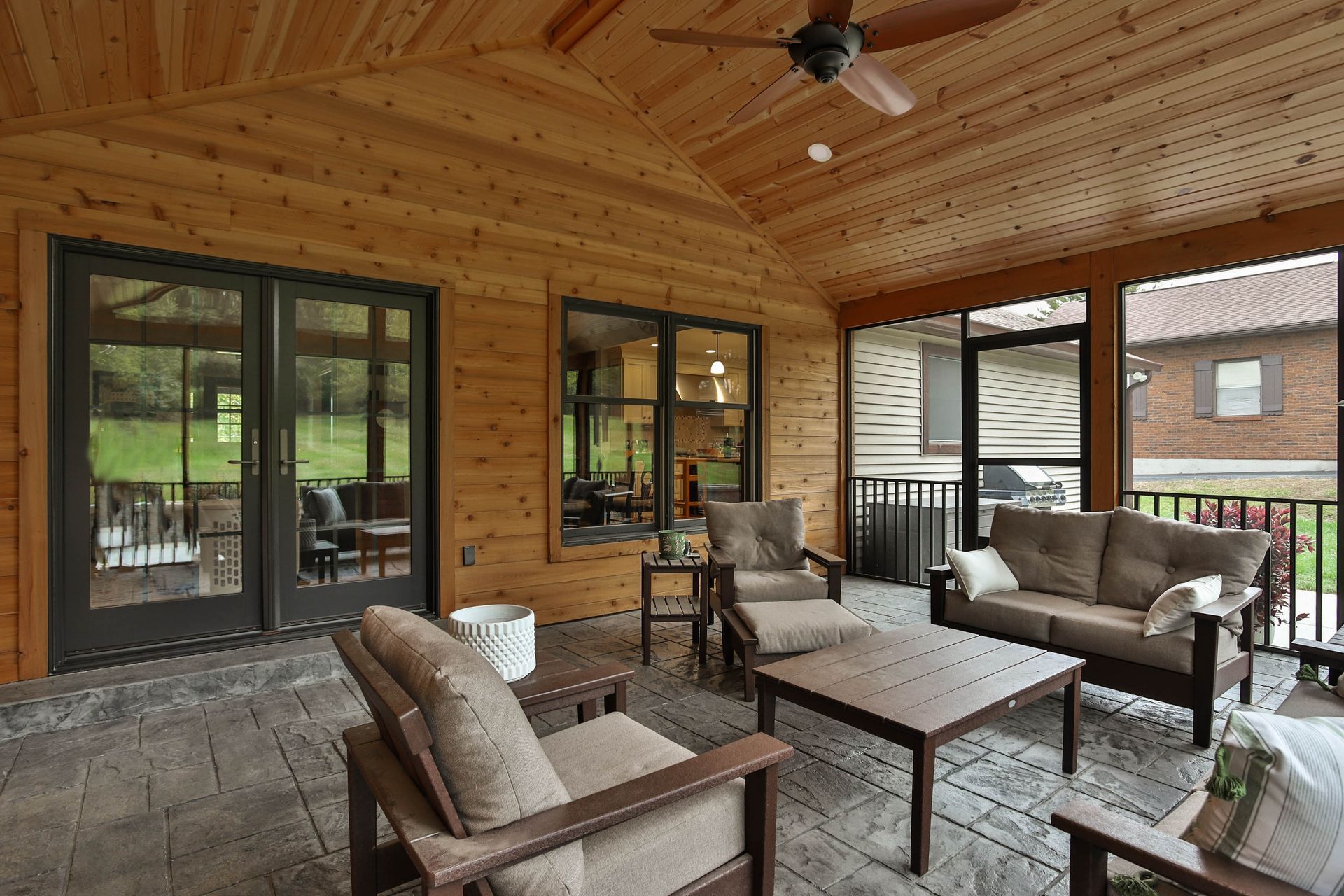 A screened-in porch with a couch, chairs, tables, and a ceiling fan