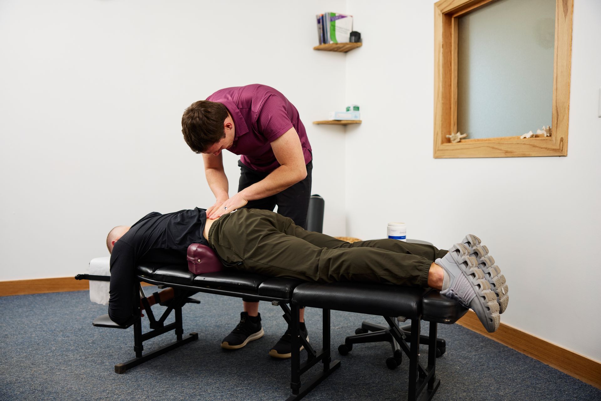 Chiropractor adjusting a patient lying face down on a treatment table in a clinic room.