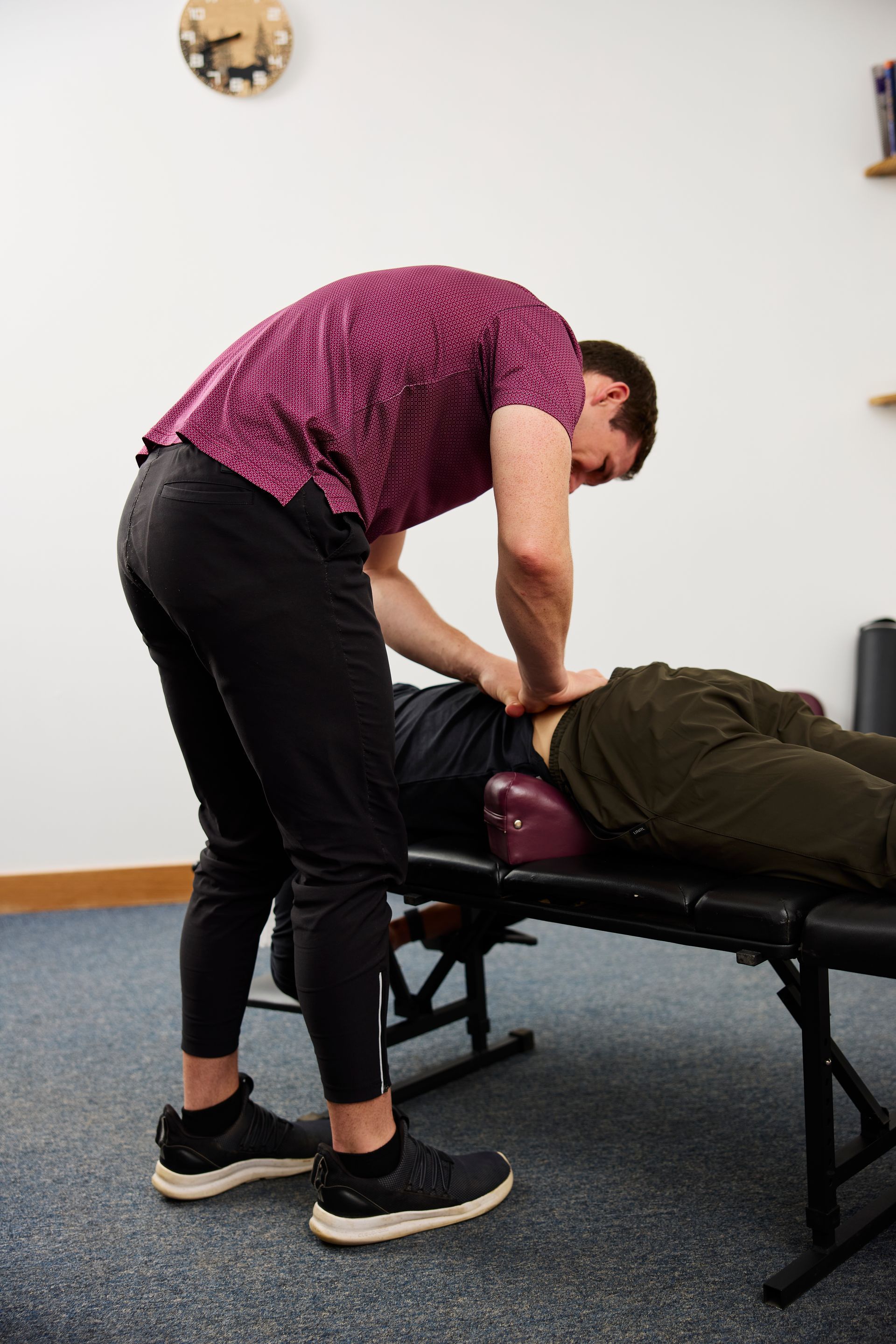 Therapist adjusts a person lying face down on a treatment table in a clinic room.