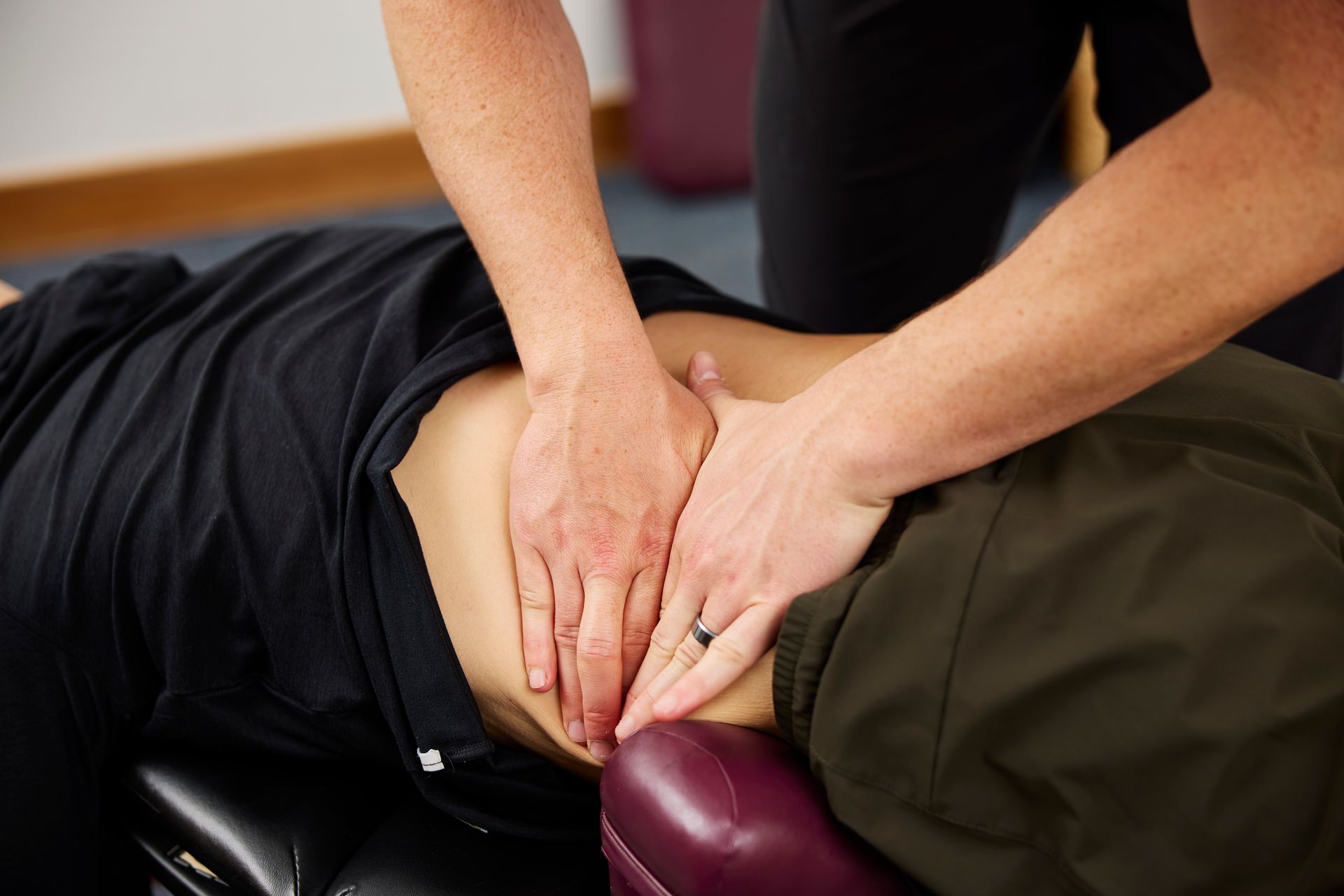 Hands performing a chiropractic adjustment on a patient’s lower back on a massage table.