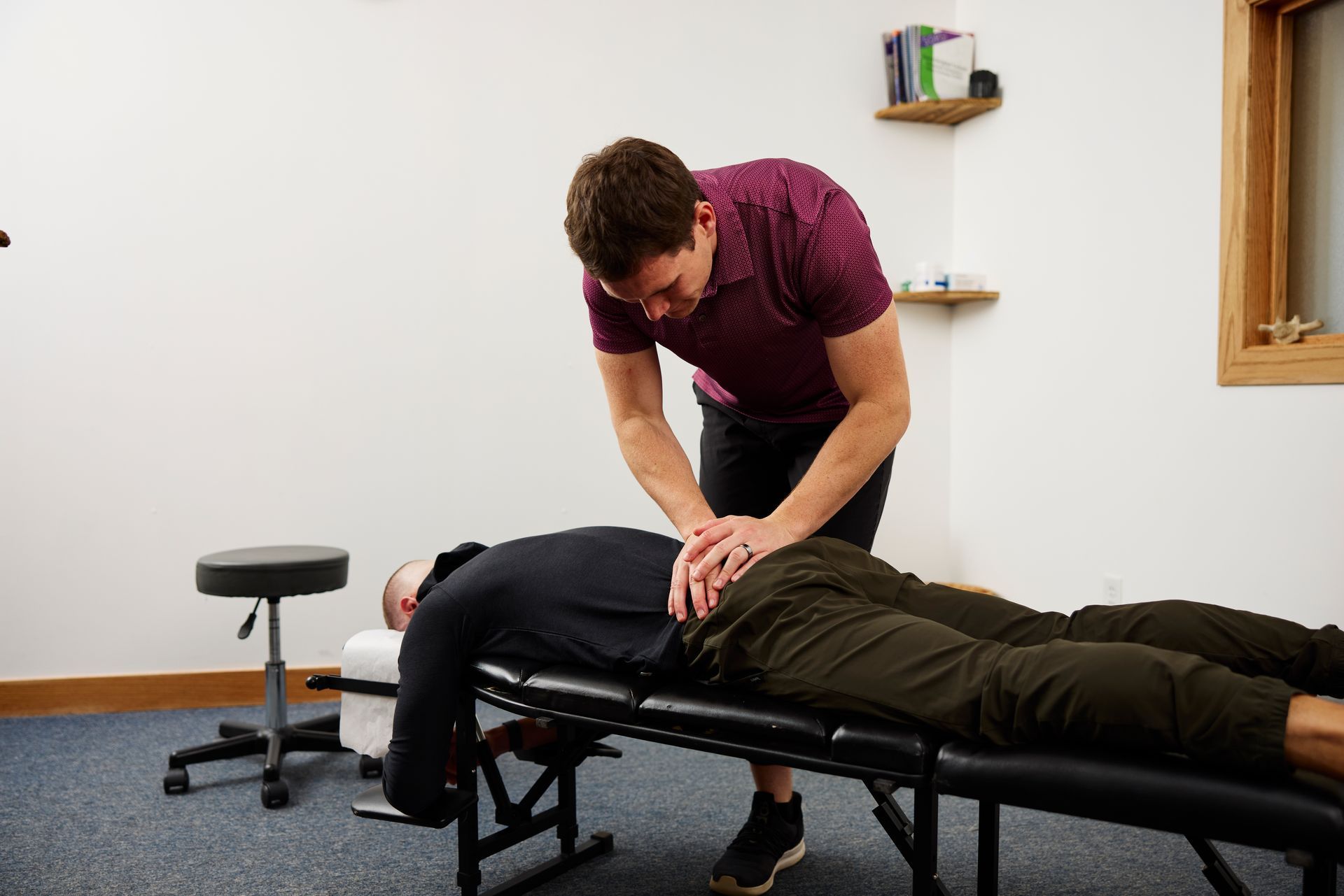 Chiropractor adjusting a patient lying on a treatment table in a clinic room.