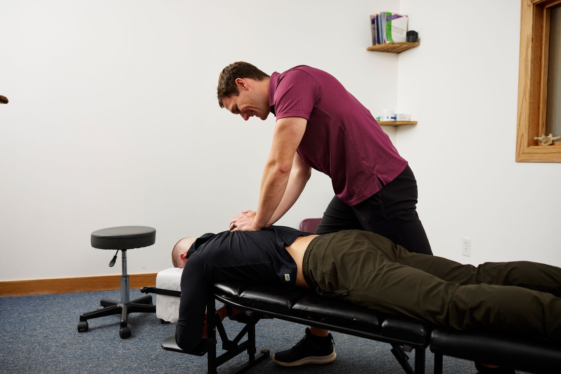 Therapist performing a back adjustment on a patient on a treatment table in a clinic room.