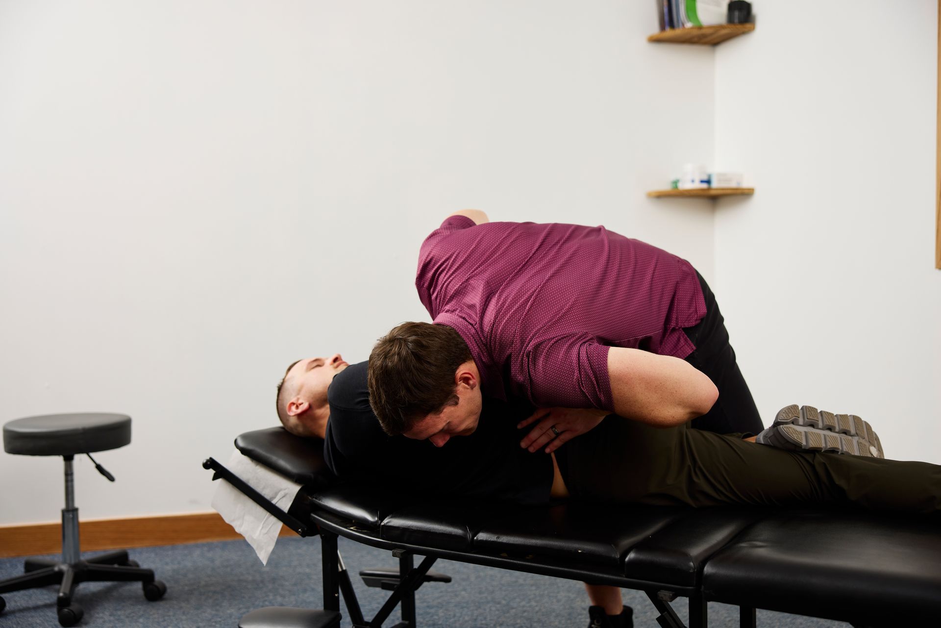 Chiropractor adjusting a patient on a treatment table in a clinic room.