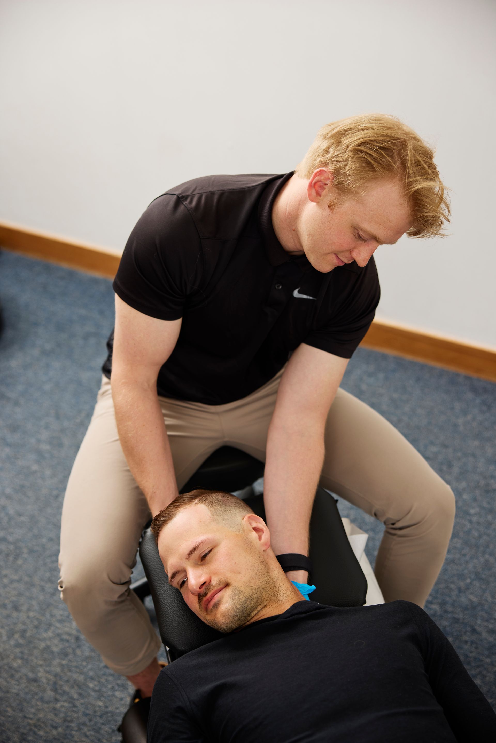 Two people practicing a neck massage on a blue carpet in a room.