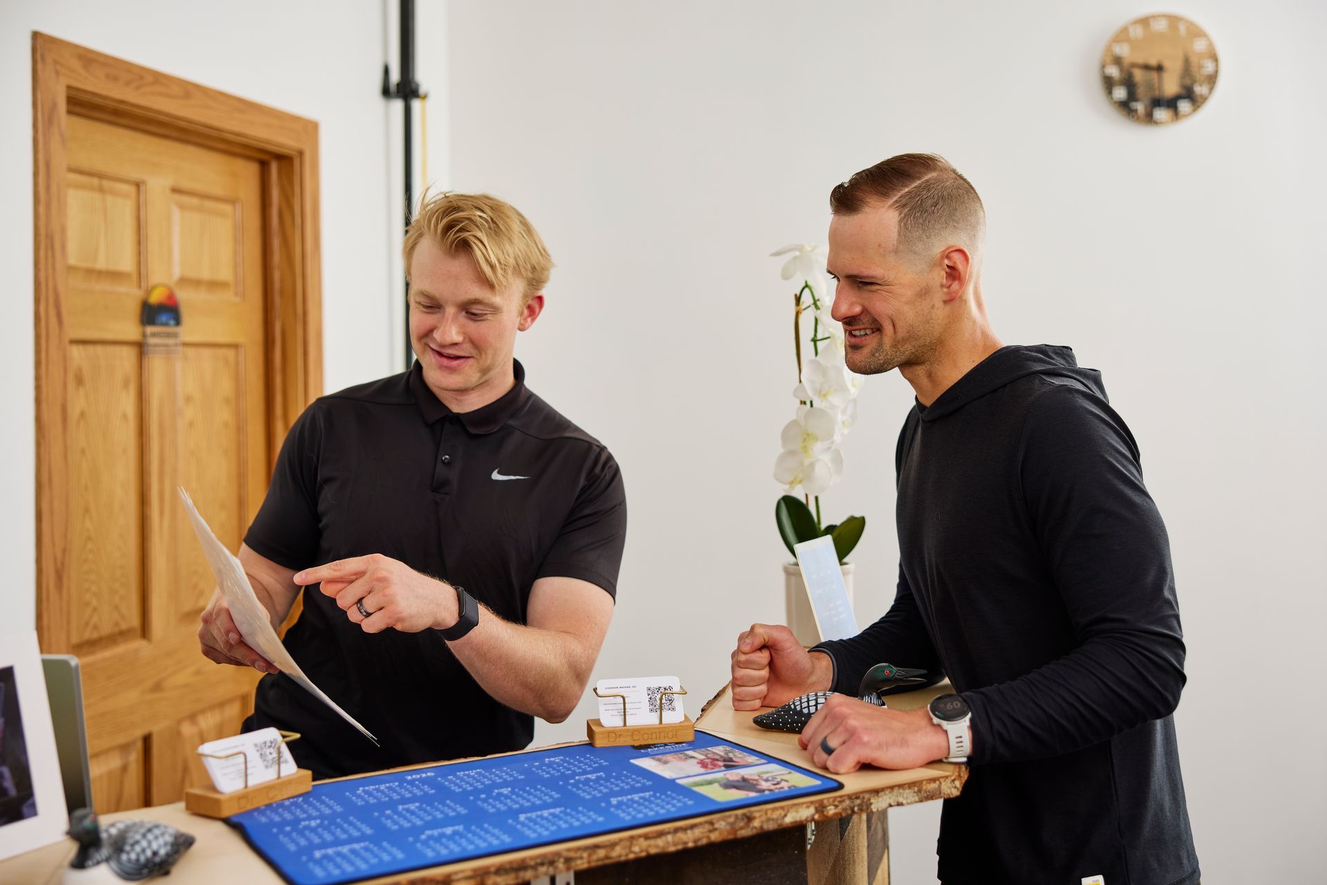 Two men in black shirts reviewing items at a counter in a bright room.
