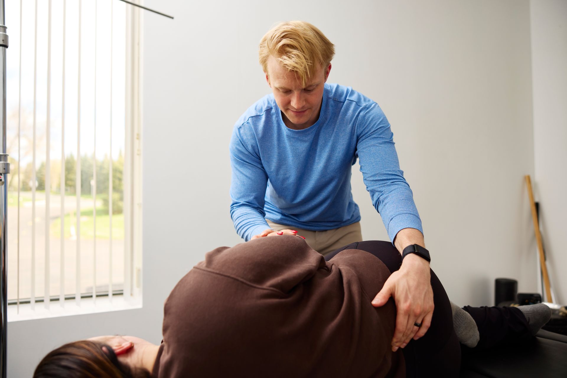 Therapist adjusting a client lying face down during a treatment session in a bright room.