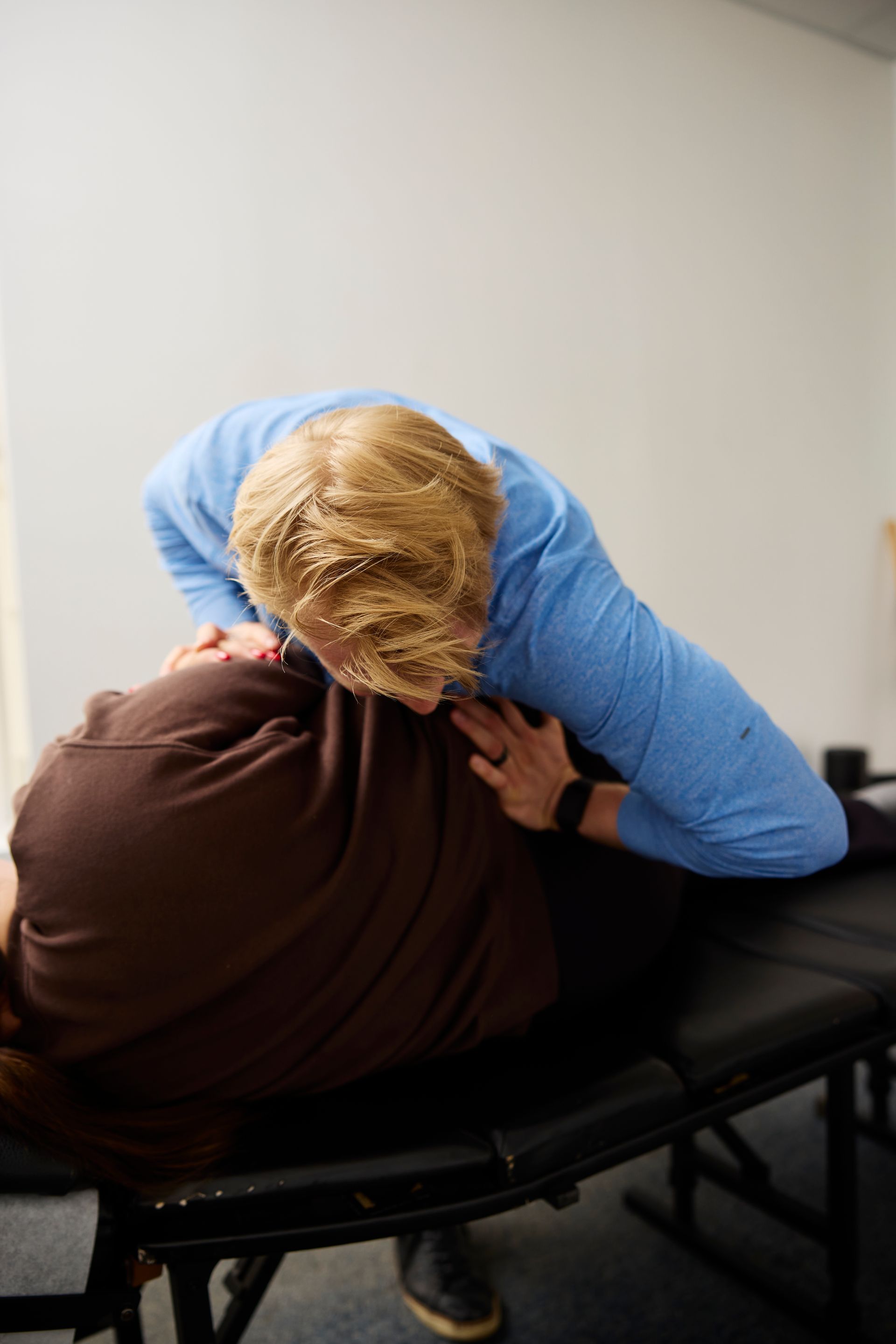 Person in a blue shirt performing a chiropractic adjustment on a patient lying face down on a treatment table.