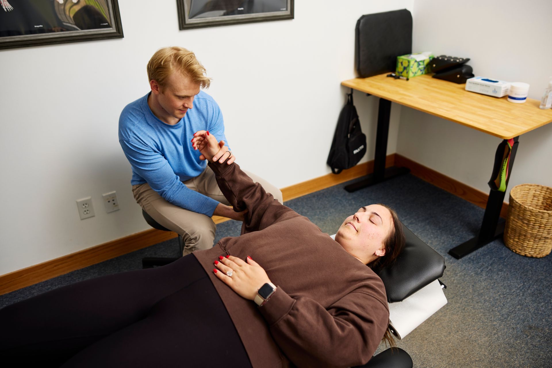 Two people in a therapy room, one helping the other do a leg stretch on a treatment table.