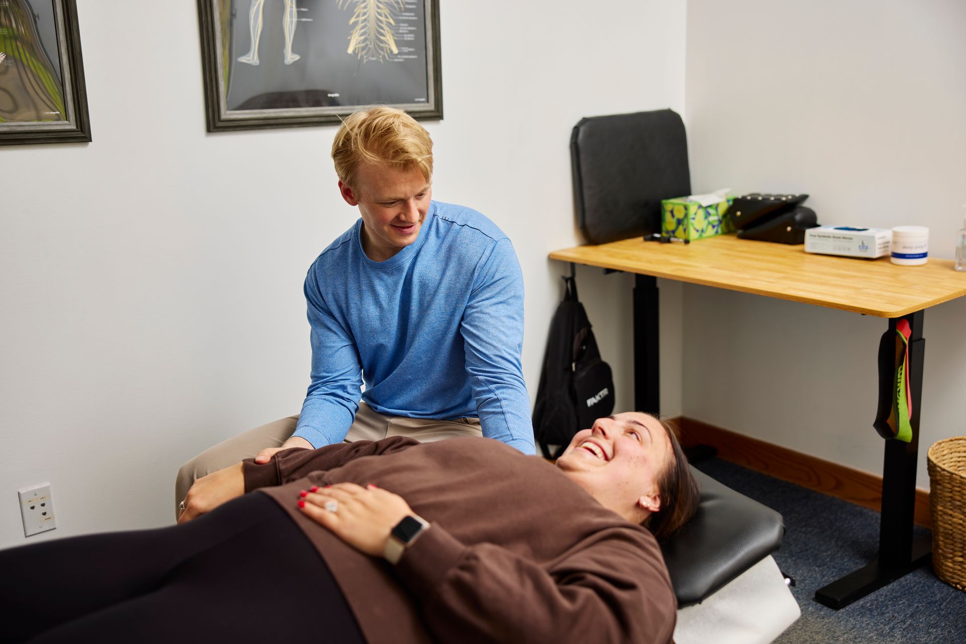 A clinician examines a patient lying on a treatment table in a small office.