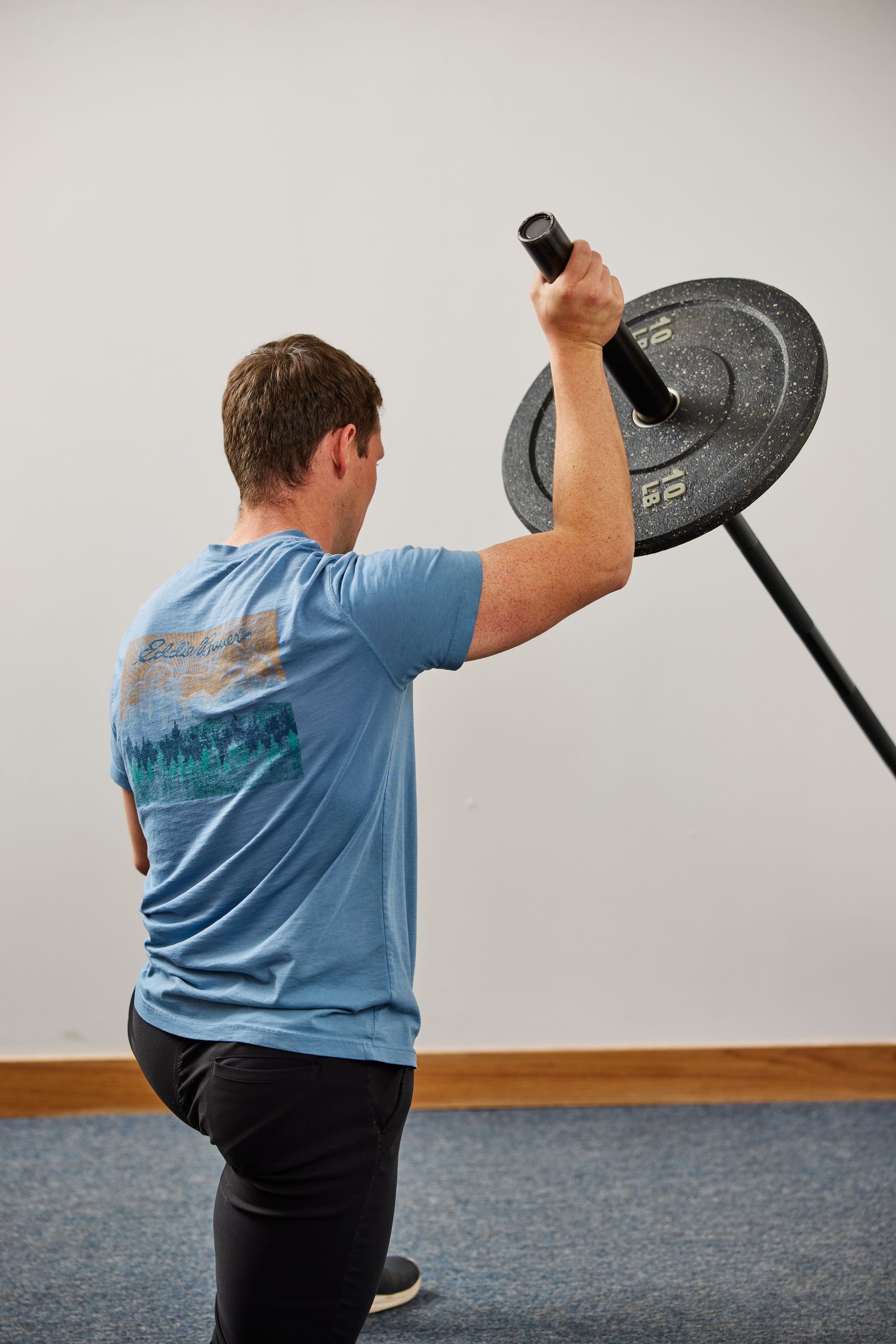 Person exercises with a landmine barbell in a gym, holding a black plate overhead.