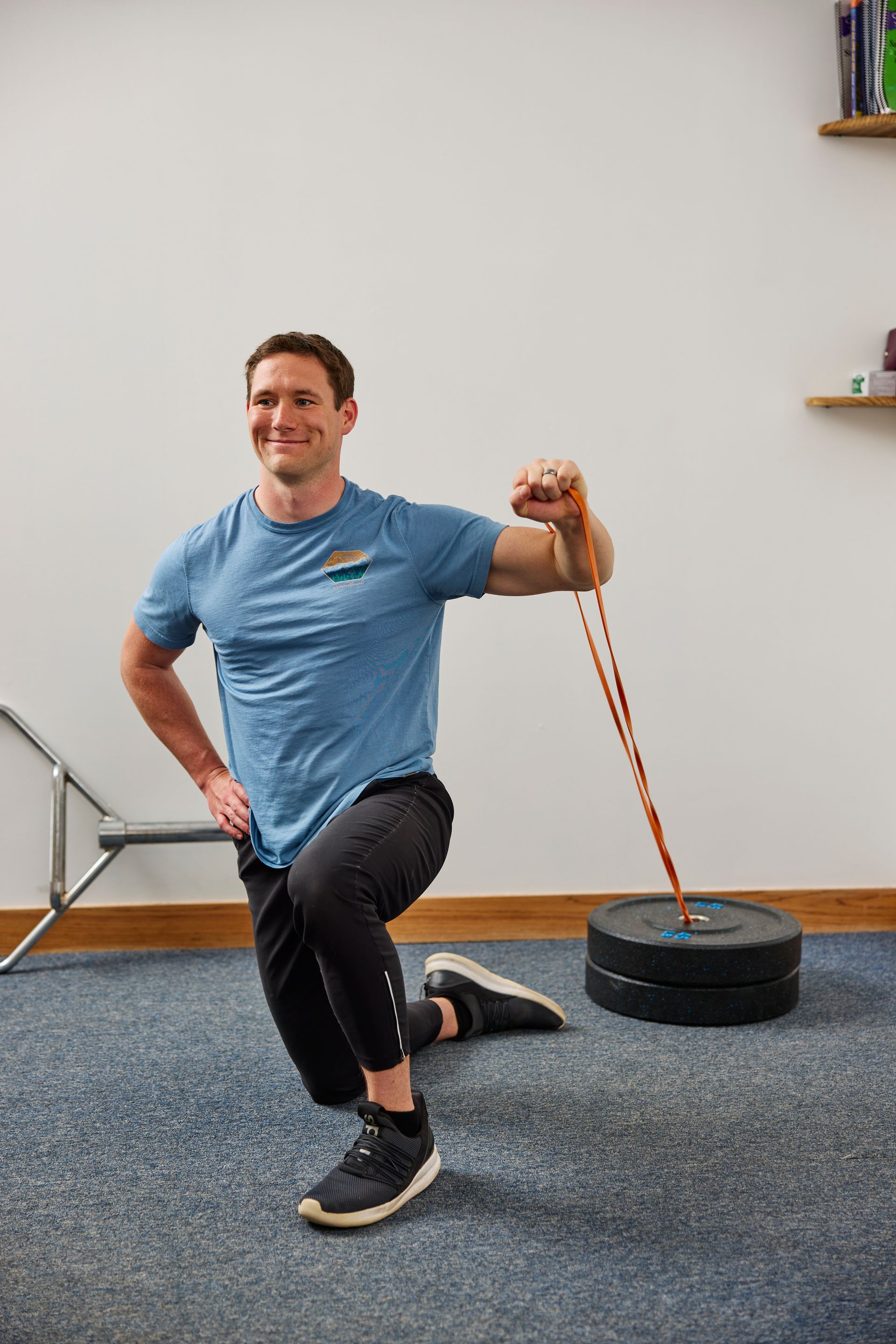 Man kneeling in a gym, holding resistance bands attached to a weight plate.