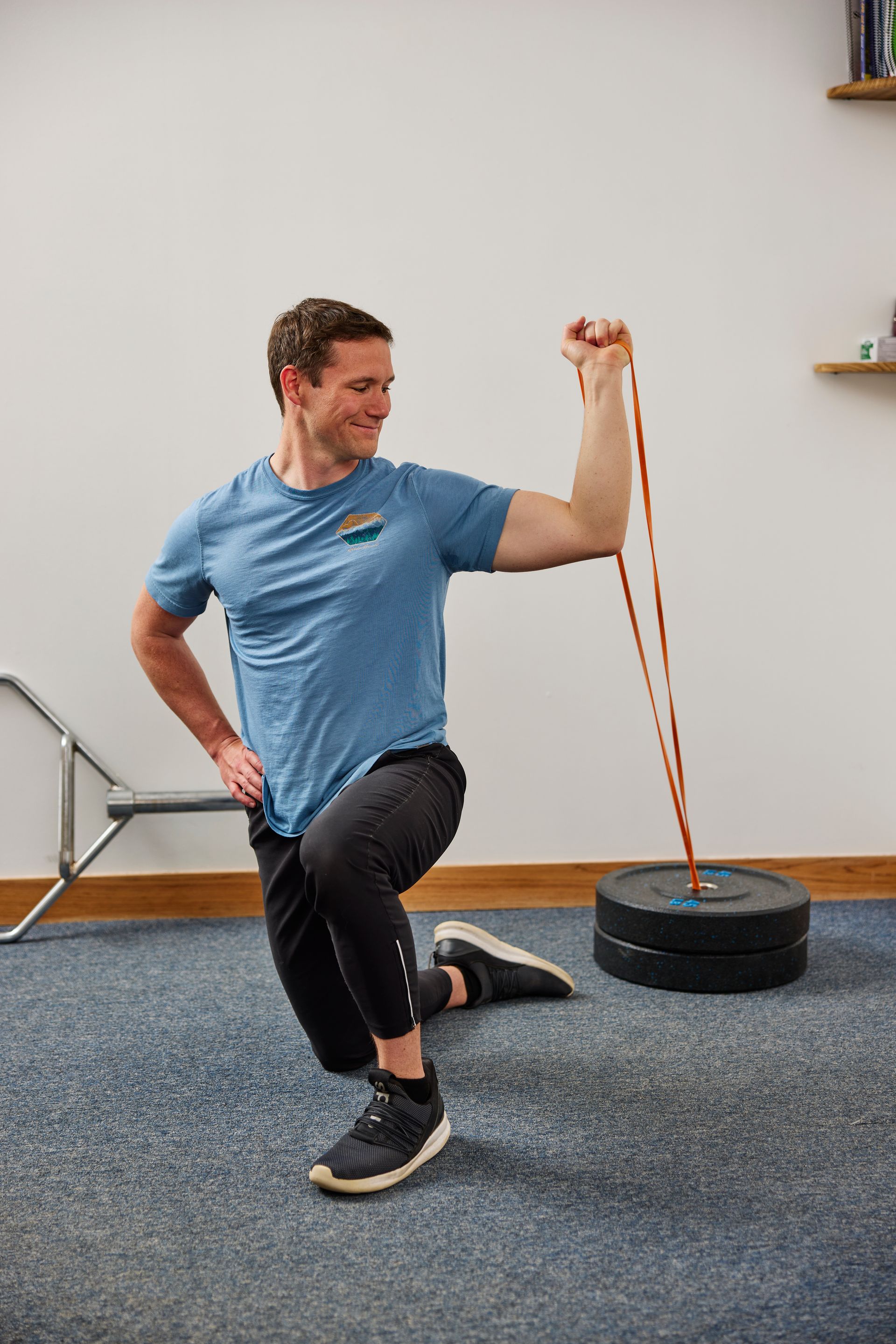 Man exercising with resistance band in a gym, kneeling beside a weighted anchor.