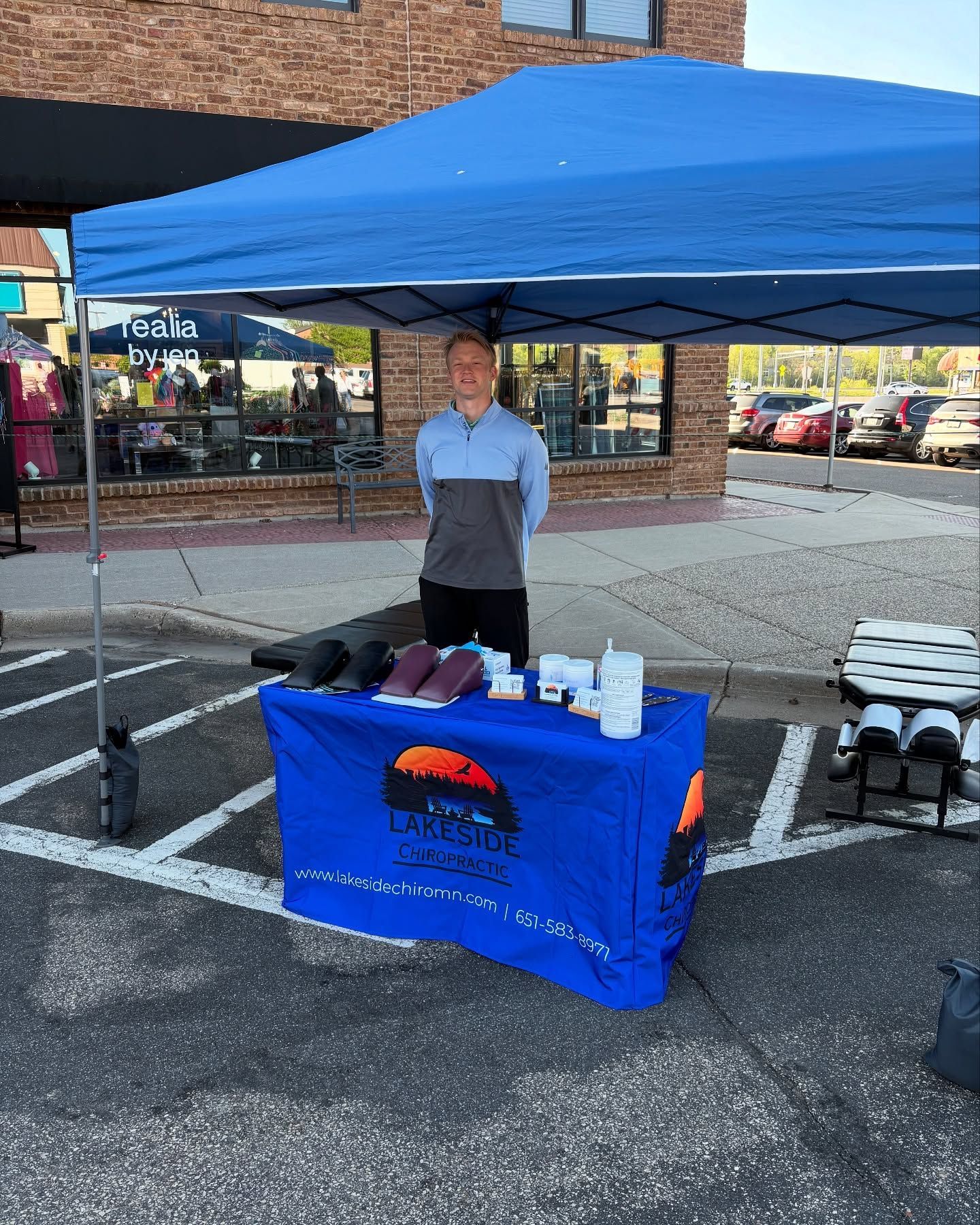 Person behind a blue canopy table at an outdoor event, with brochures and cups displayed.