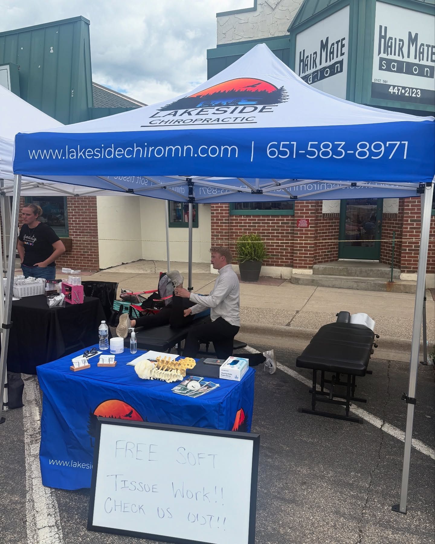 A Lakeside Chiropractic pop-up tent on a street with staff assisting a person on a massage table.
