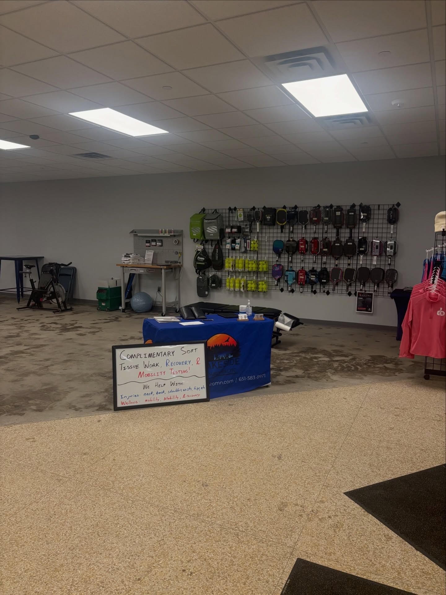 A registration desk with a sign sits in an indoor space with a display wall of merchandise and fitness equipment.