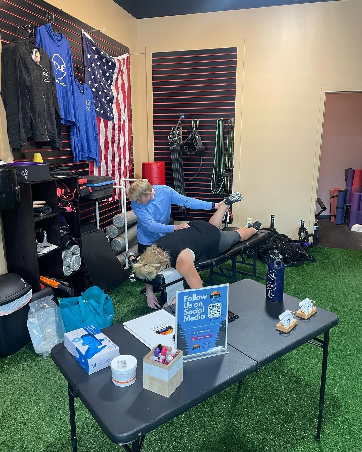 A practitioner performs manual therapy on a person lying face down on a treatment table inside an office or gym space.
