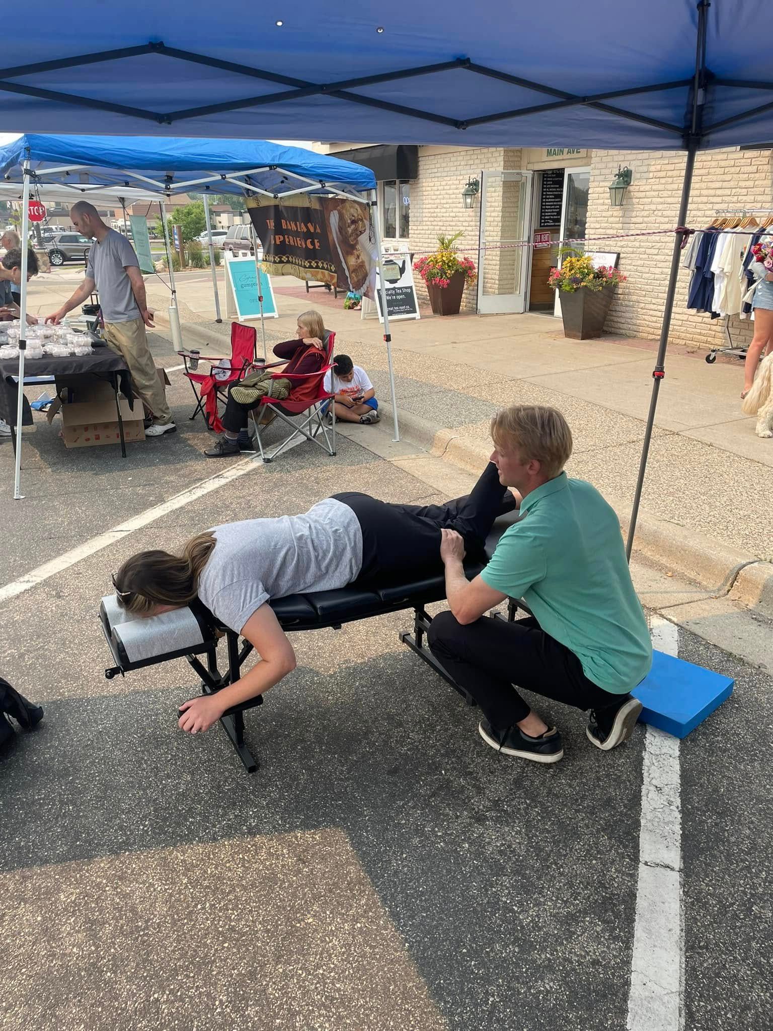 A practitioner performs a chiropractic adjustment on a person lying prone on a portable table at an outdoor event.