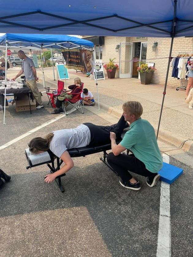 A practitioner performs a chiropractic adjustment on a person lying prone on a portable table at an outdoor event.