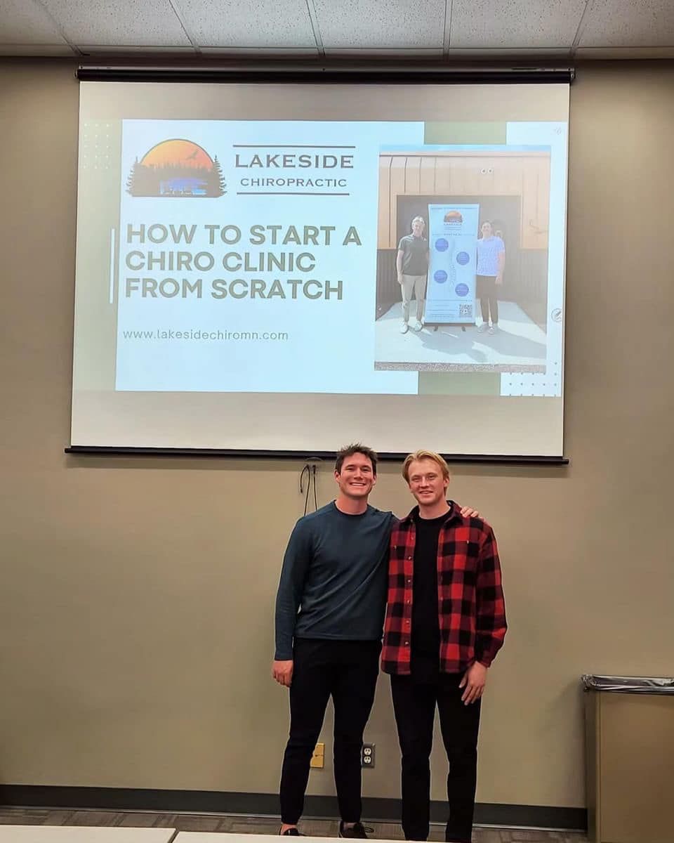 Two people standing in front of a projected slide about starting a chiropractic clinic from scratch.