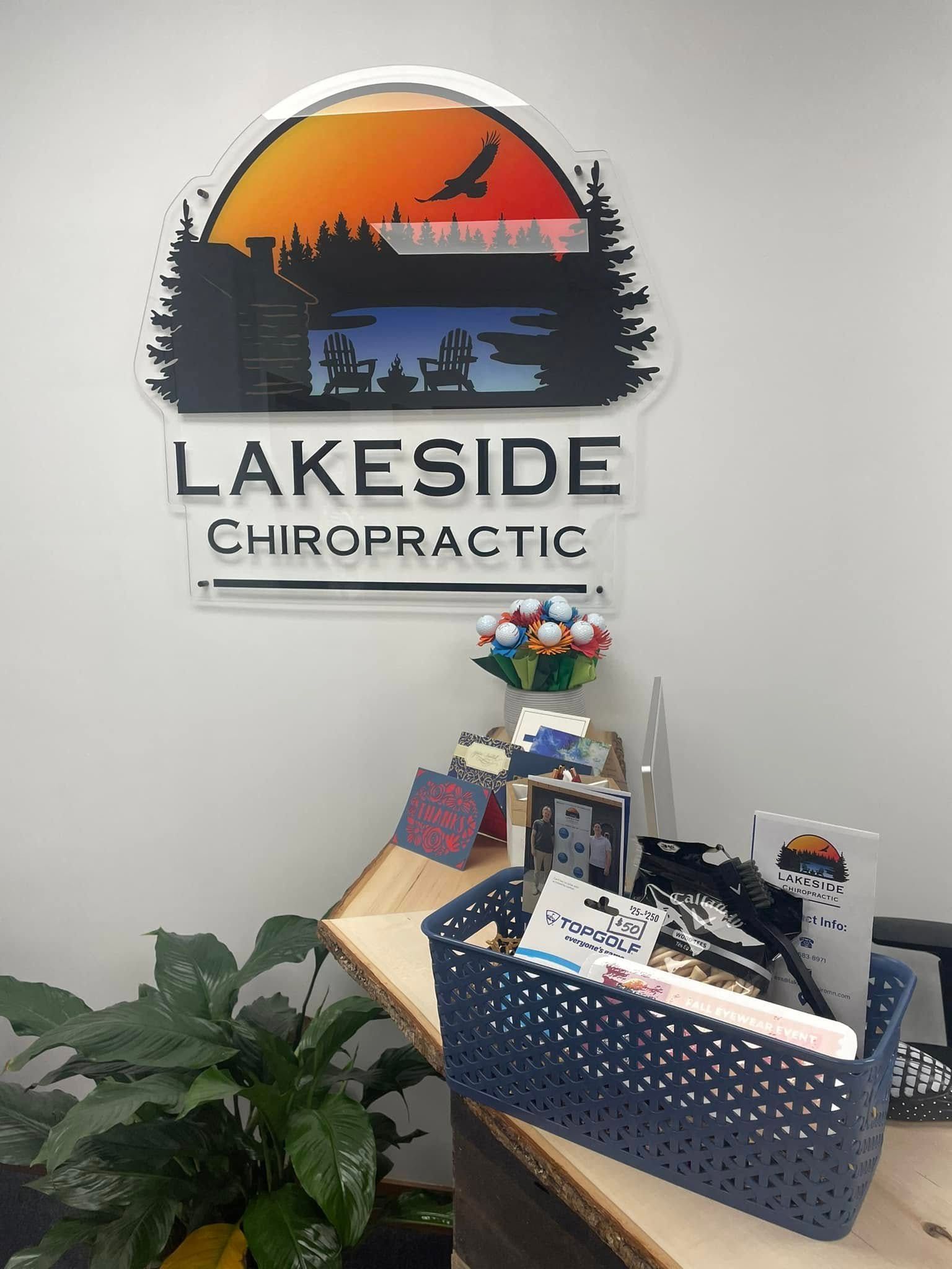 Lakeside Chiropractic sign on a white wall above a wooden desk with a plant and a blue bin containing office supplies.
