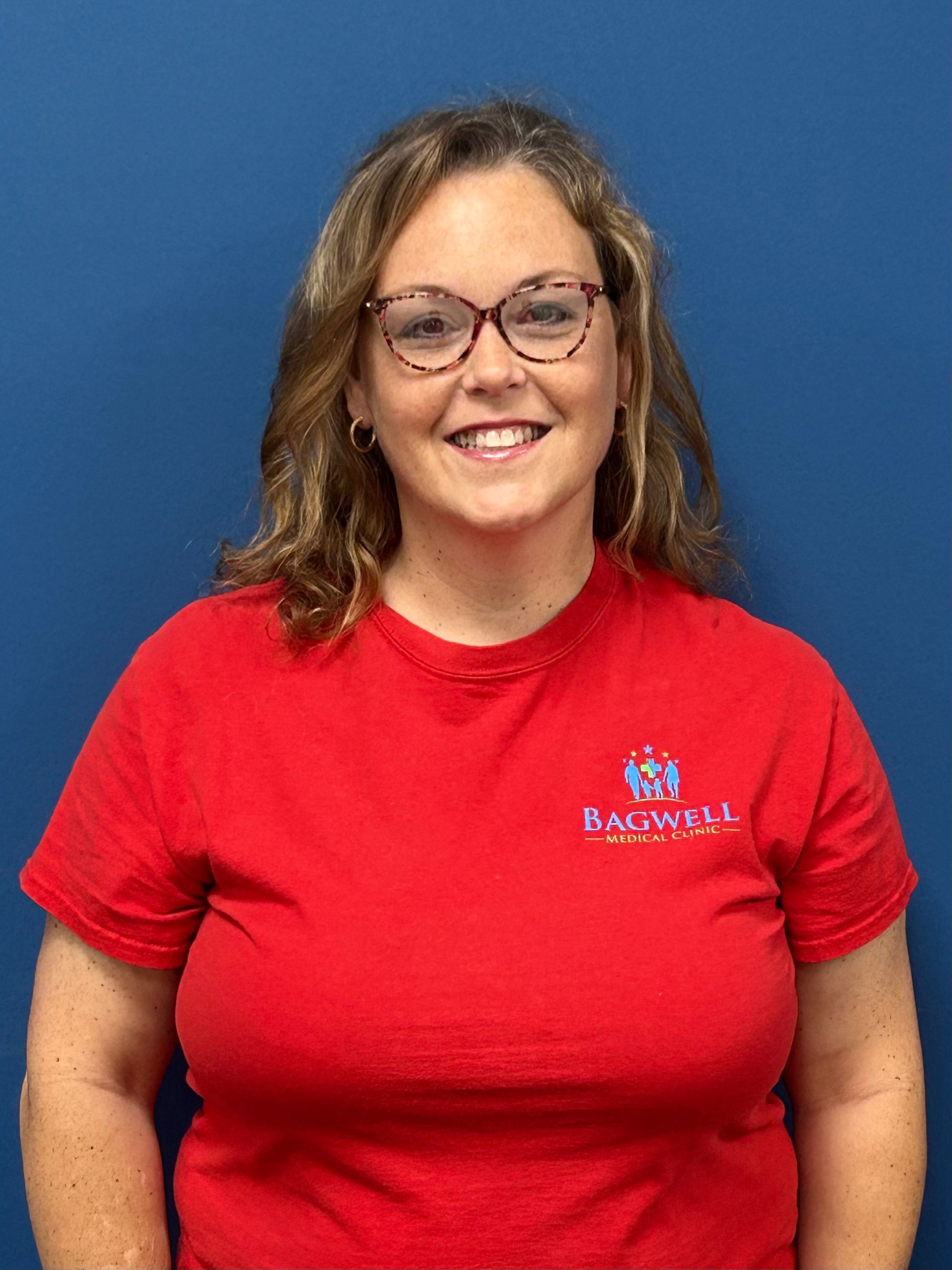 A woman wearing glasses and a red shirt is smiling for the camera.