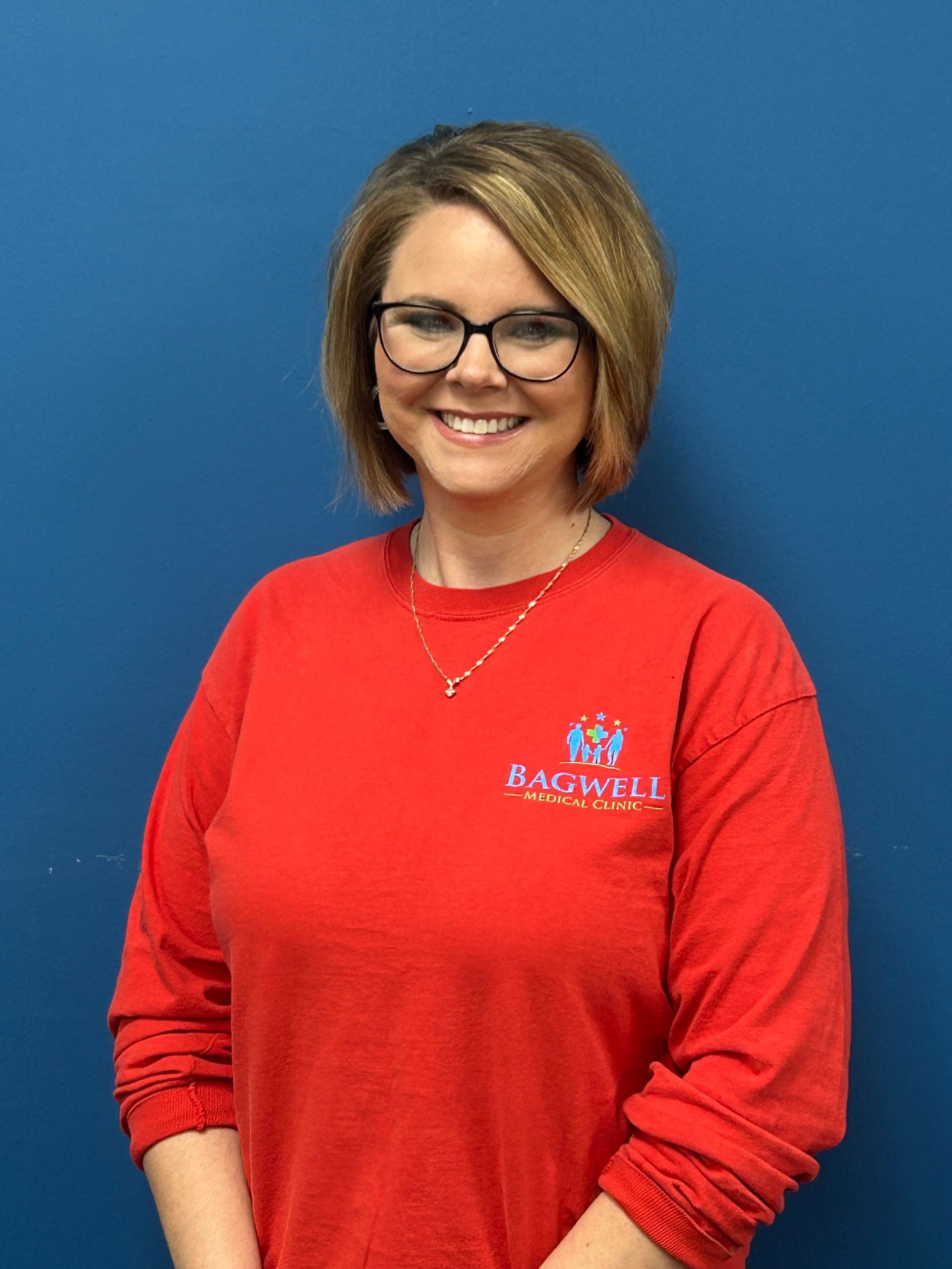 A woman wearing glasses and a red shirt is standing in front of a blue wall.