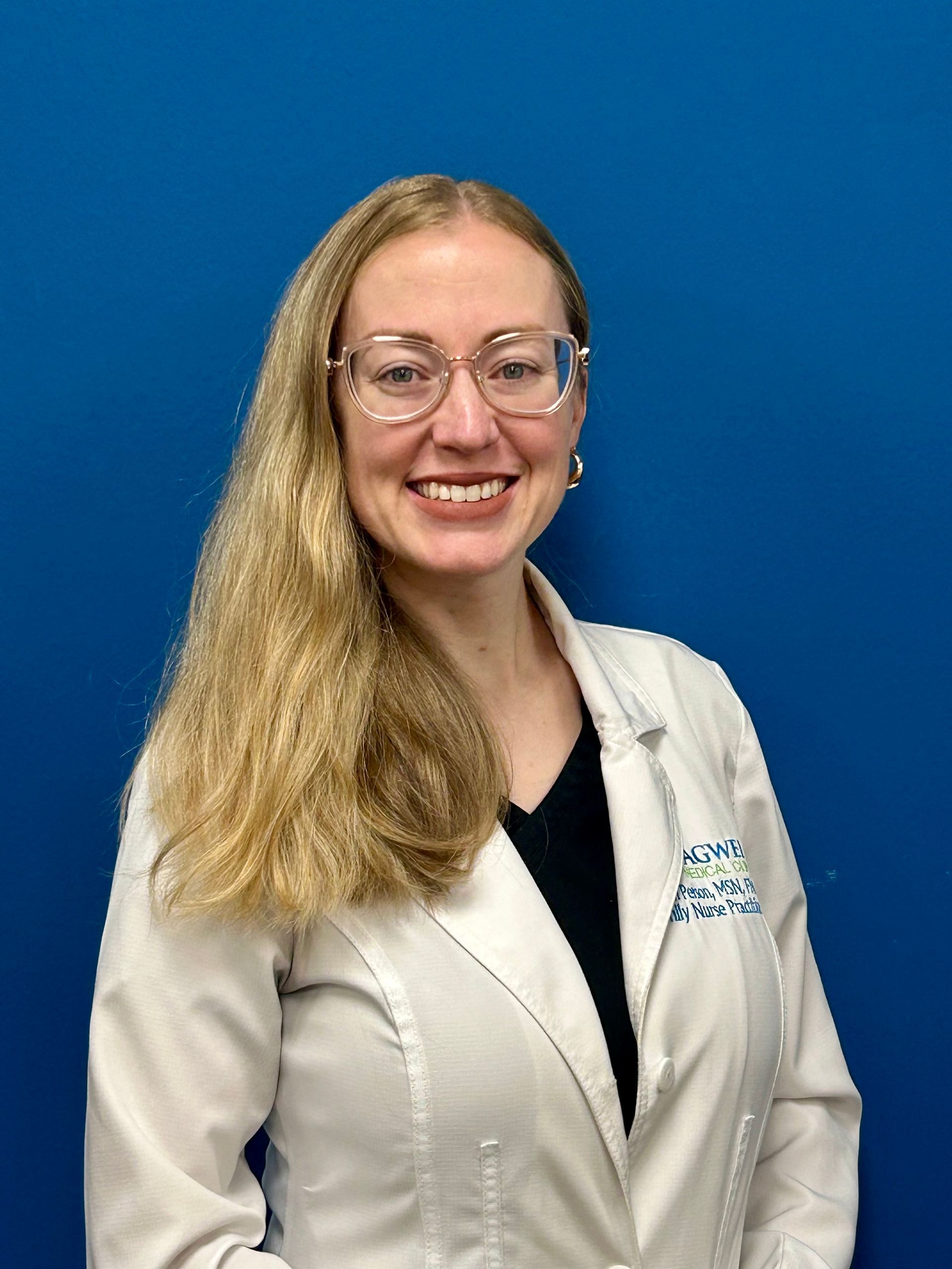 A woman in a white lab coat and glasses is smiling in front of a blue background.