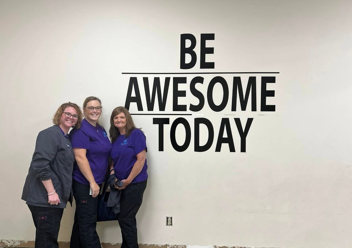 Three women are standing in front of a wall that says `` be awesome today ''.