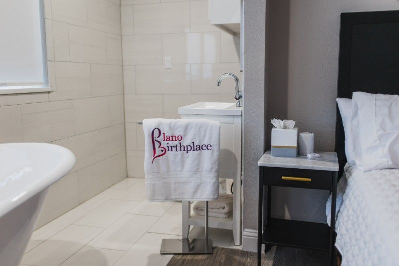 A bathroom with a bathtub , sink , nightstand and bed.