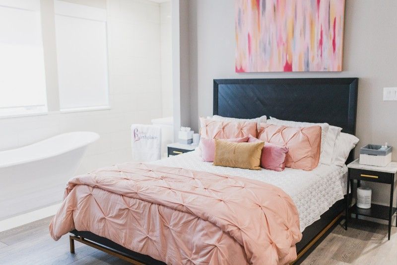 A bedroom with a bed , nightstands , a bathtub and a painting on the wall.