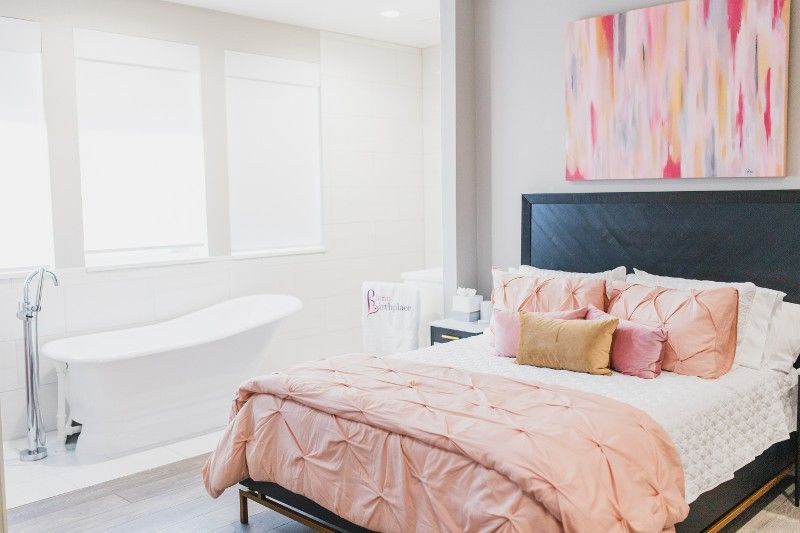 A bedroom with a bed , bathtub and painting on the wall.