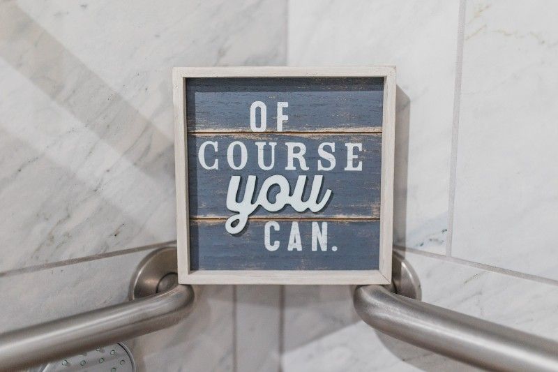 A sign that says `` of course you can '' is hanging on a bathroom railing.