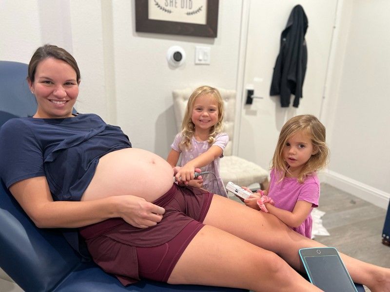 A pregnant woman is sitting in a chair with two little girls.