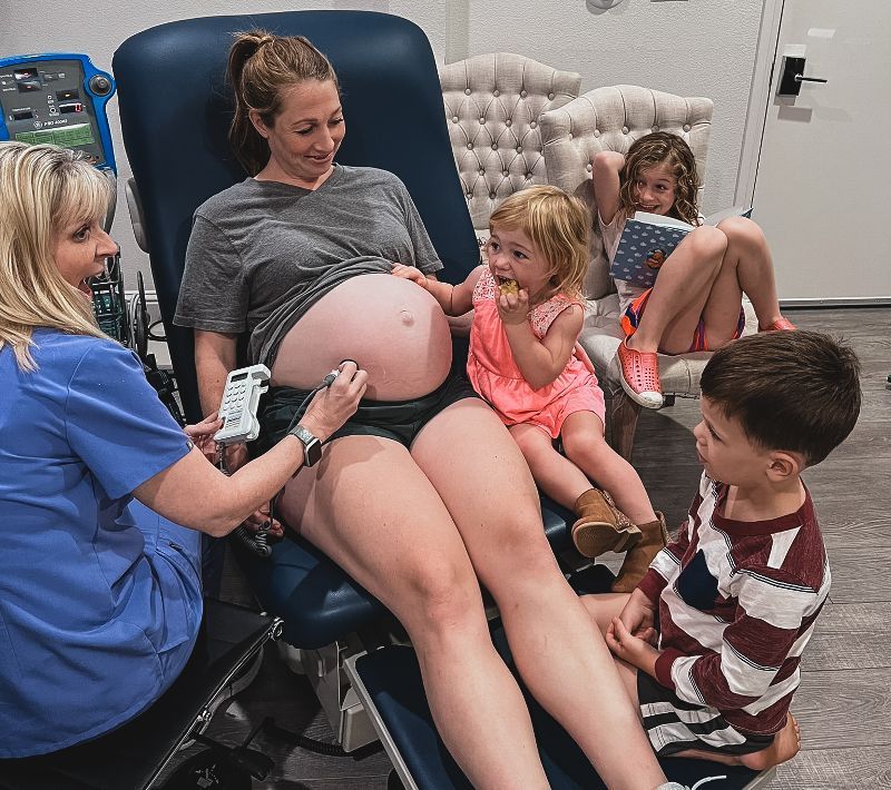 A woman checking on a pregnant woman with child beside her