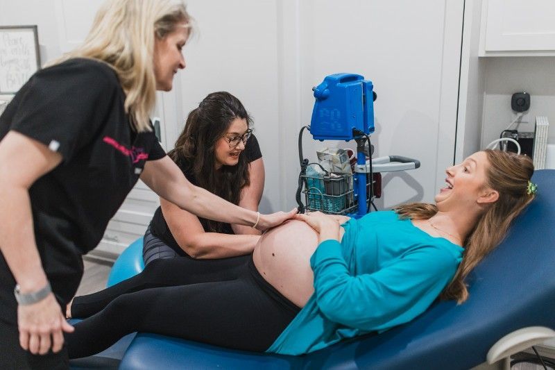 A pregnant woman is laying on a bed with two women standing around her.
