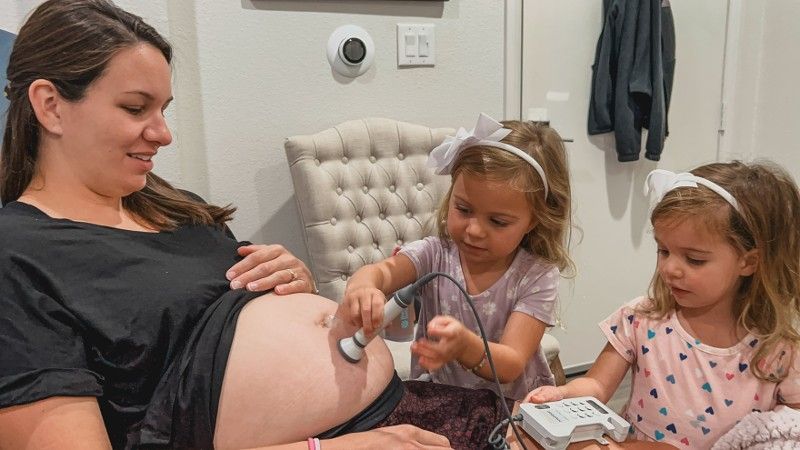 A pregnant woman is being examined by two little girls who are playing doctors.