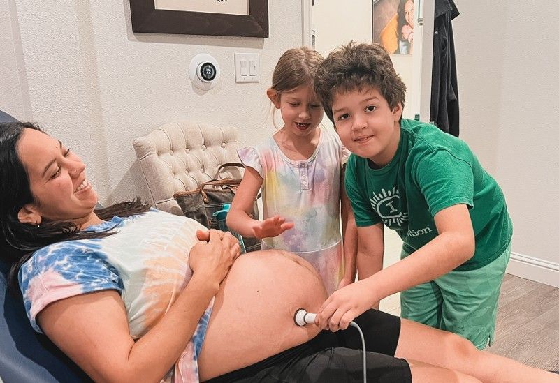 Two children are standing next to a pregnant woman.