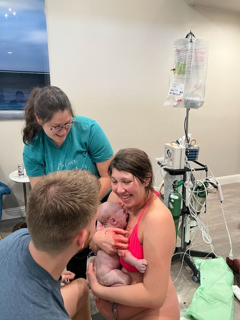 A woman is holding a baby in her arms while a man looks on.