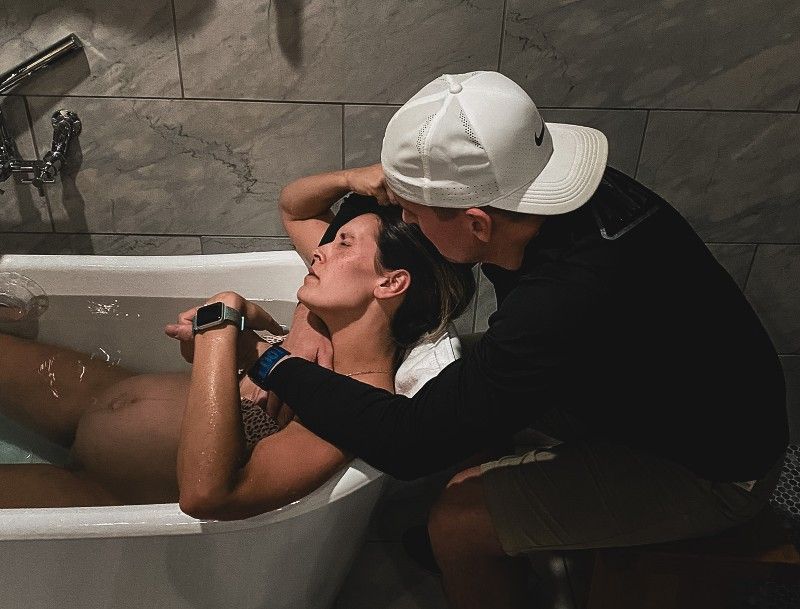 A man is kneeling next to a woman in a bathtub.