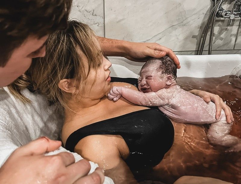 A woman is holding a newborn baby in a bathtub.