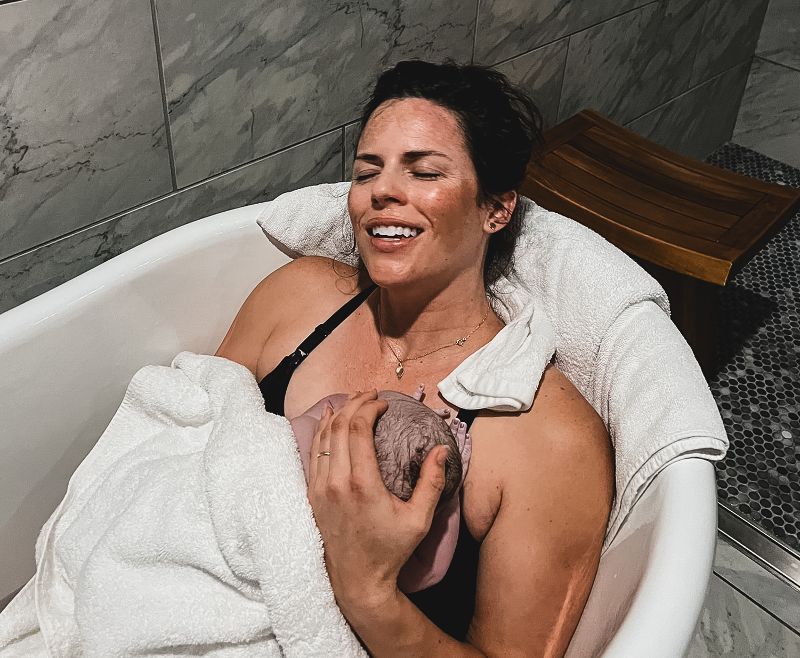 A woman is holding a newborn baby in a bathtub.