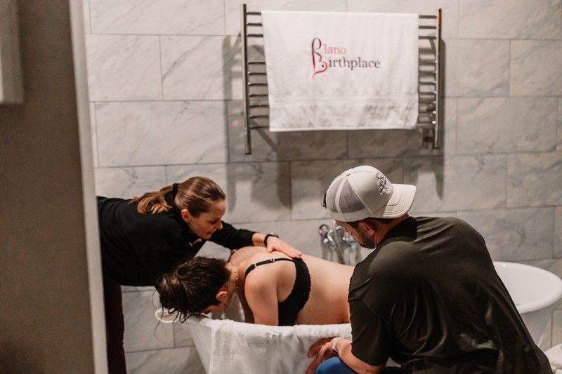 A woman helping a pregnant woman while her husband is beside her