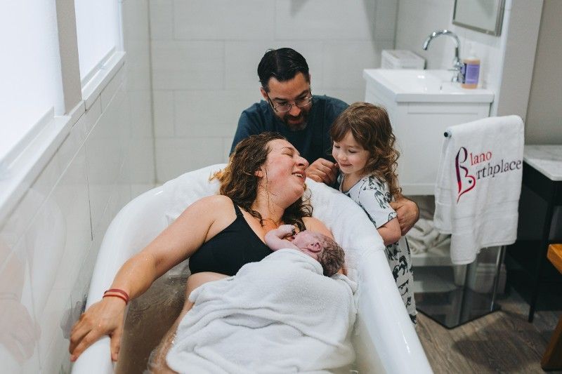 A woman is giving birth in a bathtub with her husband and two children.