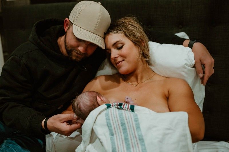A man and a woman are holding a newborn baby in a hospital bed.
