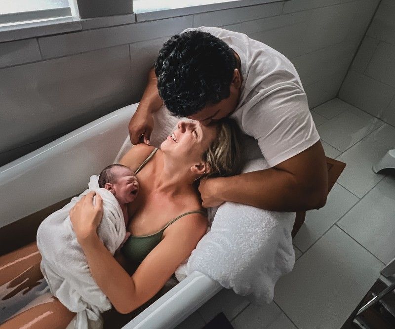 A man and a woman are holding a newborn baby in a bathtub.