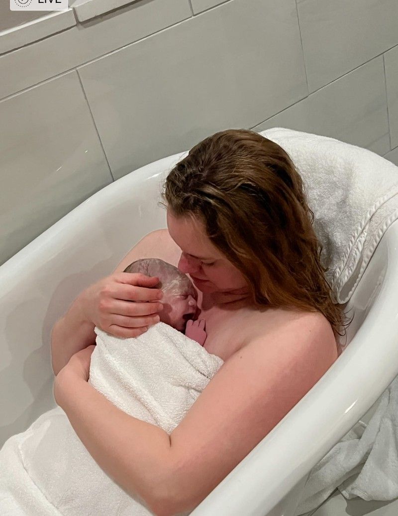 A woman is holding a newborn baby in a bathtub