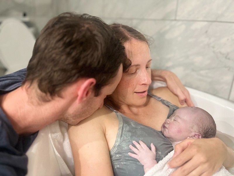 A man and woman are holding a newborn baby in a bathtub.