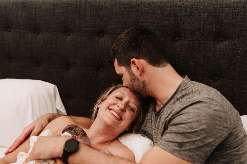 A man and a woman are laying on a bed holding a newborn baby.