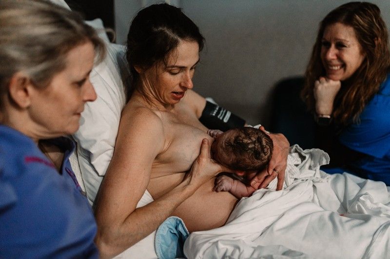 A woman lactating and breast feeding her baby while people assisting her
